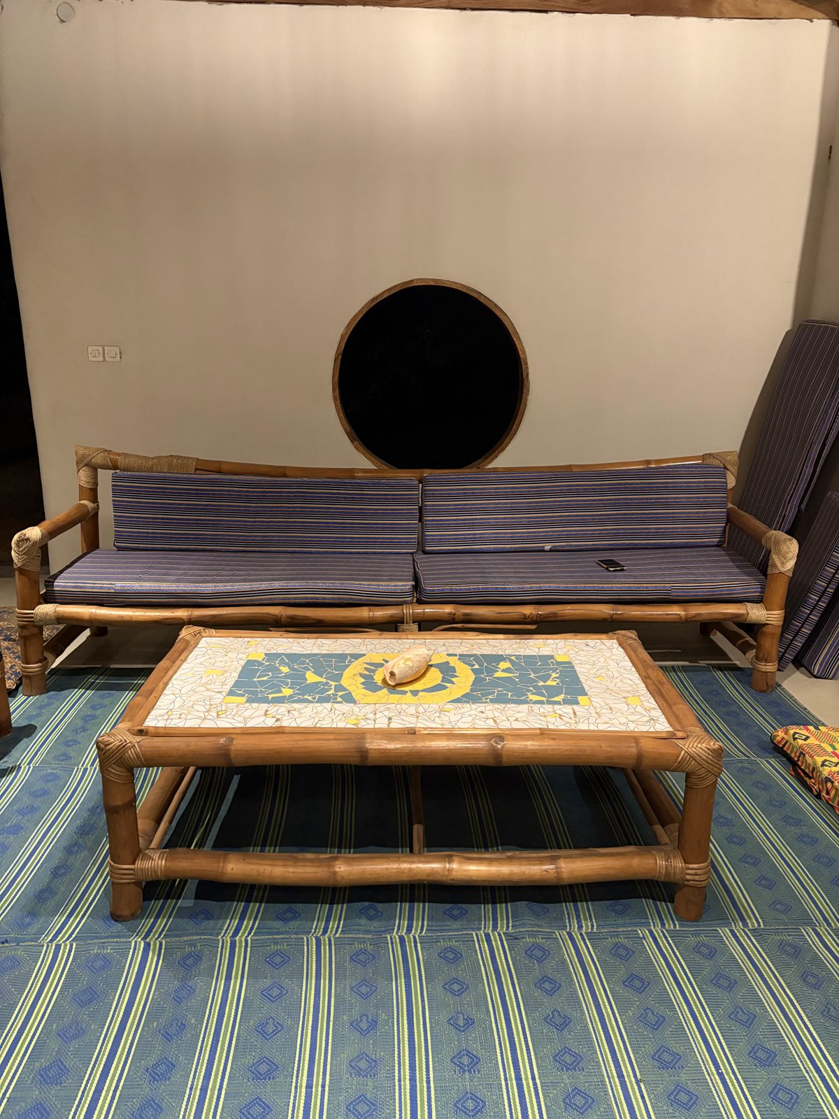 Bamboo sofa and a mosaic coffee table on a blue woven mat in front of a round window