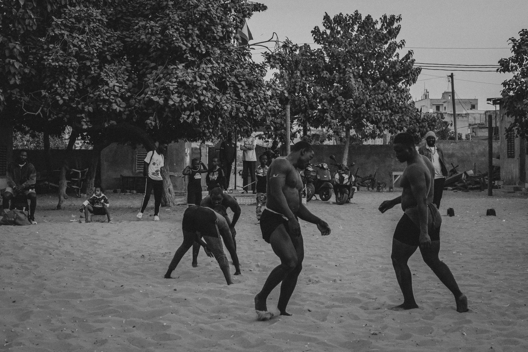 Wrestlers practising in the sand under trees, children watching