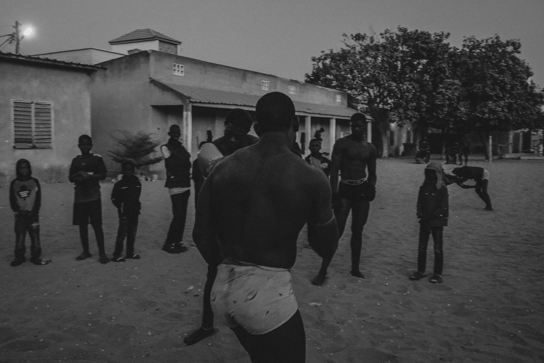 A wrestler seen from behind facing a group of boys at dusk