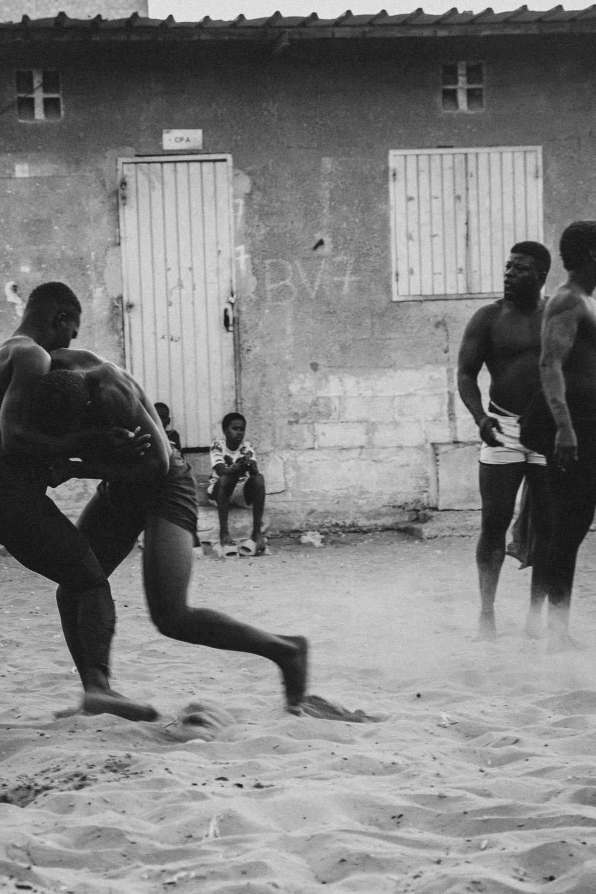 Two wrestlers in motion raising dust while others watch
