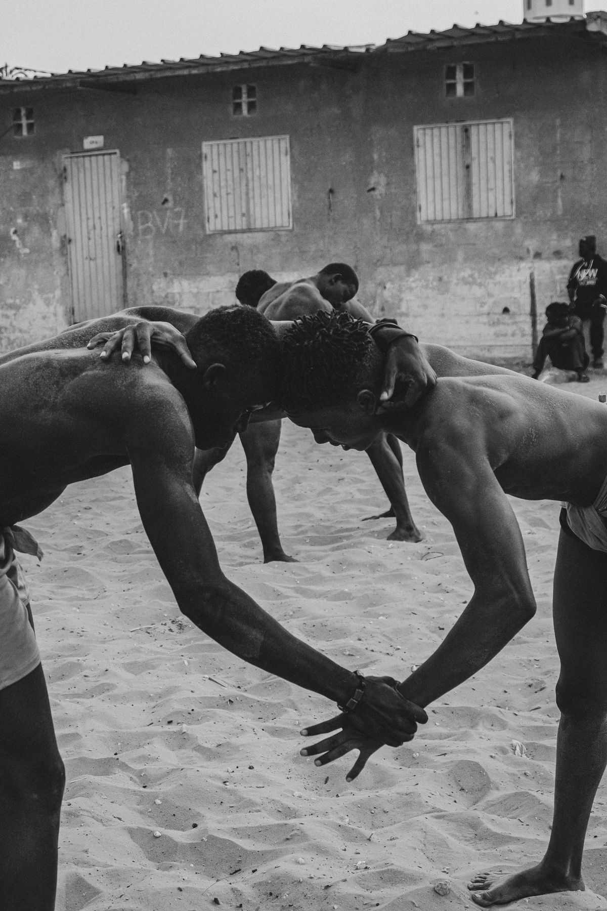 Two wrestlers touching heads, hands clasped, others training behind