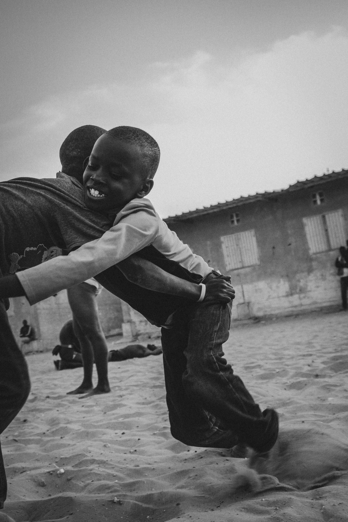 Two boys wrestling, one laughing, in the sand