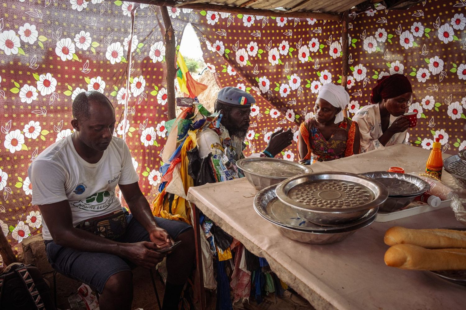 L’Homme Plastique sits and talks with three people in a tent of flowered fabric